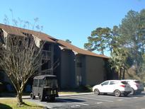 Exterior view of the two-story condo building with parking, landscaping, and an adjacent golf cart at 207 Indian Wells Ct. # 207, Murrells Inlet, SC 29576