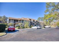 A condo building exterior with parking, lush trees, and blue sky at 207 Indian Wells Ct. # 207, Murrells Inlet, SC 29576