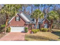 Charming brick home featuring a two-car garage, palm trees, and meticulously manicured landscaping at 48 Heston Ct., Pawleys Island, SC 29585
