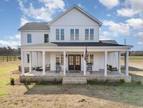 Front exterior of a stunning two-story home with a welcoming porch, rocking chairs, and an American flag at 11455 W Highway 19, Loris, SC 29569