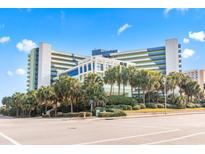 Bright and airy exterior view of a modern beachfront resort with lush palm trees and manicured landscaping at 1105 S Ocean Blvd. # 604, Myrtle Beach, SC 29577