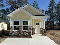 Charming yellow home featuring stone accents, white trim, and a well-manicured lawn under a clear blue sky at 3135 Tiger Tail Rd., Conway, SC 29526