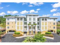 Stunning condo building with light yellow and white exterior, lush landscaping, and palm trees at 1352 Villa Marbella Ct. # 1-104, Myrtle Beach, SC 29572