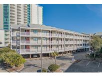 Exterior view of condo building with multiple floors, white railings, parking underneath, and a view of a high-rise building at 210 North Ocean Blvd. # 330, North Myrtle Beach, SC 29582