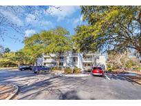 Condo exterior with mature trees, multiple units, parking area, and well maintained landscape and blue skies at 415 Ocean Creek Dr. # 2359, Myrtle Beach, SC 29572