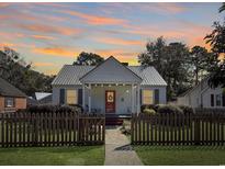Charming cottage-style home with a metal roof, a picket fence, and a cozy front porch, set against a beautiful sunset backdrop at 632 Magnolia Dr., Georgetown, SC 29440