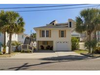 Charming two-story beach home featuring a garage, outdoor seating, and beautiful landscaping with palm trees at 513 Hillside Dr. S, North Myrtle Beach, SC 29582