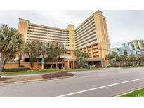 Spacious condo building with yellow facade, parking garage and view of the street at 6900 N Ocean Blvd. # 1008, Myrtle Beach, SC 29572