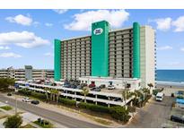 View of the Royal Garden Resort showcasing its balconies, parking garage, and oceanfront location with palm trees and a blue sky at 1210 N Waccamaw Dr. # 305, Murrells Inlet, SC 29576