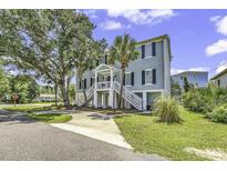Charming raised beach home with dual staircases and covered entry, surrounded by mature trees and landscaping at 1519 N Palmetto Dr., Surfside Beach, SC 29575