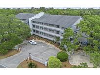 An exterior view of a condo with a parking lot, surrounded by lush greenery and trees at 310 5Th Ave. N # 206, Surfside Beach, SC 29575