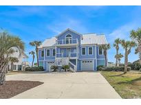 Beautiful blue beach house featuring double garages, multiple decks, and lush tropical landscaping at 2201 S Waccamaw Dr., Murrells Inlet, SC 29576