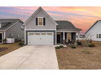 Charming home featuring a two-car garage, inviting front porch and manicured lawn set against a picturesque sunset sky at 1881 Moonseed Dr., Longs, SC 29568