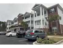 View of condo building with white balconies and brick accents, showcasing covered parking and lush landscaping at 1024 Ray Costin Way # Villa 711, Murrells Inlet, SC 29576