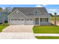 Charming exterior showcasing a gray home with a brick driveway, three-car garage, and well-manicured lawn at 1413 Crooked Hook Rd., North Myrtle Beach, SC 29582