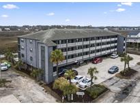 Condo building featuring covered parking, palm trees, and balconies with white railings at 123 N Dogwood St. # 107, Garden City Beach, SC 29576
