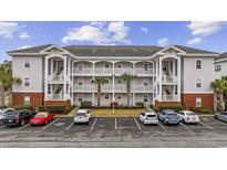 Three-story condo with white balconies, palm trees, and ample parking in a well-maintained community at 4142 Hibiscus Dr. # 104, Little River, SC 29566