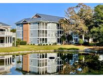 Water view of condo building with blue siding, green lawn, three floors of screened in porch and lush foliage at 4637 Lightkeepers Way # 4-A, Little River, SC 29566