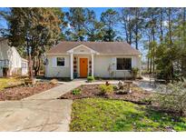 Charming home featuring a cheerful orange door and a well-manicured garden, surrounded by lush greenery and mature trees at 6420 Spice Bush Crescent, Myrtle Beach, SC 29588