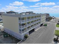 Wide exterior shot of a four story condo complex with multiple balconies by the ocean under a bright blue partly cloudy sky at 301 N Waccamaw Dr. # 209, Garden City Beach, SC 29576