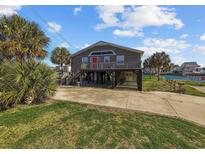 Inviting raised beach house with a red door, spacious driveway, and lush tropical landscaping at 310 37Th Ave. N, North Myrtle Beach, SC 29582