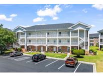 Three-story condo building with white balconies, brick accents, parking spaces, and landscaped lawn at 3927 Gladiola Ct. # 101, Myrtle Beach, SC 29588