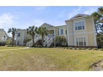 Attractive two-story condo building with yellow siding, white trim, a lawn and a stairway entrance at 77 Tern Pl. # 202, Pawleys Island, SC 29585