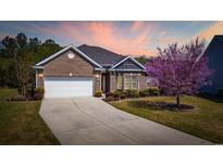 Beautiful brick home with a two car garage, manicured lawn, and lovely landscaping under a colorful sunset sky at 1112 Raven Cliff Ct., Conway, SC 29526