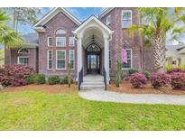Elegant brick home featuring a covered front entrance with white columns, complemented by lush landscaping at 653 Whispering Pines Ct., Murrells Inlet, SC 29576