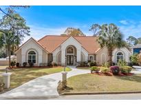 Charming single-story home featuring a tile roof, arched entryway, circular driveway, and lush landscaping at 5628 Marion Circle, Myrtle Beach, SC 29577