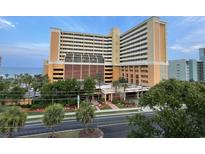 Beautiful view of a peach and beige beachfront condo building, with palm trees, ocean, and blue sky at 6900 N Ocean Blvd. # 1505, Myrtle Beach, SC 29572