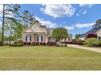 Beautiful brick home featuring mature landscaping, a sprawling green lawn, and elegant black shutters at 9278 Nw Checkerberry Square, Calabash, NC 28467