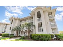 Beautiful multi-story condo building featuring white trim, balconies, palm trees, and manicured landscaping at 4409 Eastport Blvd. # E2, Little River, SC 29566