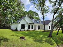 Charming, newly built white farmhouse-style home boasts a neatly manicured green lawn and black framed windows at 974 Crooked Oak Dr., Pawleys Island, SC 29585
