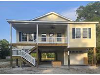 Charming yellow coastal home with a large front porch, white railings, and a ground-level garage at 4831 Riverside Dr., North Myrtle Beach, SC 29582