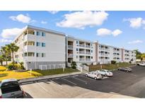 Four-story condo building with white exterior, multiple balconies, parking lot, and palm trees at 191 Maison Dr. # B-319, Myrtle Beach, SC 29572