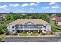 Aerial view of a condo building featuring a well-manicured lawn and ample parking surrounded by lush trees under a blue sky at 5750 Oyster Catcher Dr. # 1135, North Myrtle Beach, SC 29582