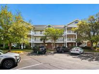 Exterior view of a three-story condo building with white balconies, lush landscaping, and ample parking at 6015 Catalina Dr. # 132, North Myrtle Beach, SC 29582
