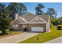 Charming brick home with attached garage, manicured lawn, mature trees, and inviting curb appeal on a sunny day at 414 Staghorn Ln., Longs, SC 29568