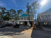 Charming raised beach house with a blue roof, nestled among lush trees in a coastal community at 6001 S Kings Hwy., Myrtle Beach, SC 29575