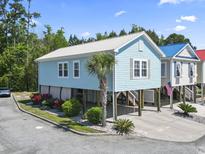 Charming raised beach house with light blue siding, metal roof, and well-manicured landscaping at 4411 Grande Harbour Blvd., Little River, SC 29566