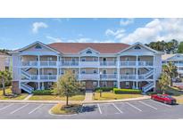 Three-story condo building featuring balconies, white railings, neat landscaping, and adjacent parking at 5750 Oyster Catcher Dr. # 234, North Myrtle Beach, SC 29582