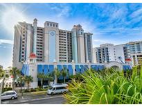 Stunning exterior view of a high-rise condo with a clock tower, blue awnings, and palm trees set against a blue sky at 2401 S Ocean Blvd. S # 267, Myrtle Beach, SC 29577