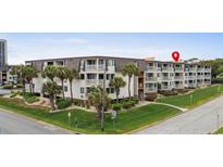 Low-rise condominium complex with landscaped grounds, mature trees, and white exterior at 5601 N Ocean Blvd. # E-304, Myrtle Beach, SC 29577