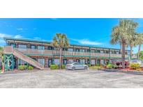 Two-story condo building with brick exterior, green trim, palm trees, and parking lot under a bright blue sky at 4516 Seaview St. # 135, North Myrtle Beach, SC 29582