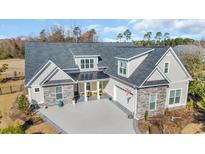 Two-story home featuring a stone and grey siding exterior, black roof, and a spacious driveway with yellow chairs on the front porch at 1004 Whooping Crane Dr., Conway, SC 29526
