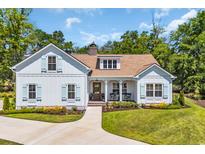 Charming farmhouse-style exterior featuring a manicured lawn, light blue shutters, and inviting front porch at 25 Northwoods Ct., Pawleys Island, SC 29585