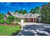 Charming brick home featuring a red door, dormer windows, lush landscaping and a curving driveway at 4363 Parkland Dr., Myrtle Beach, SC 29579