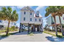 Charming stilt home with a red metal roof and light gray siding, surrounded by palm trees on a sunny day at 324 S Waccamaw Dr., Garden City Beach, SC 29576