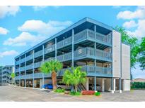 Multi-level condo building boasts ample parking, palm trees, and blue accents against a clear blue sky at 1500 Cenith Dr. # D 103, North Myrtle Beach, SC 29582